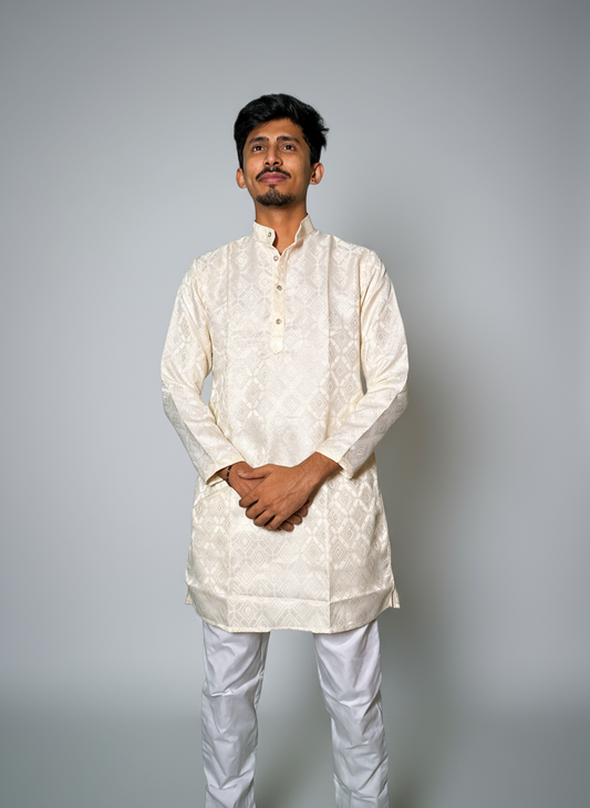 A man standing against a grey background, wearing a white jacquard kurta with a subtle pattern, full sleeves, and a band collar.